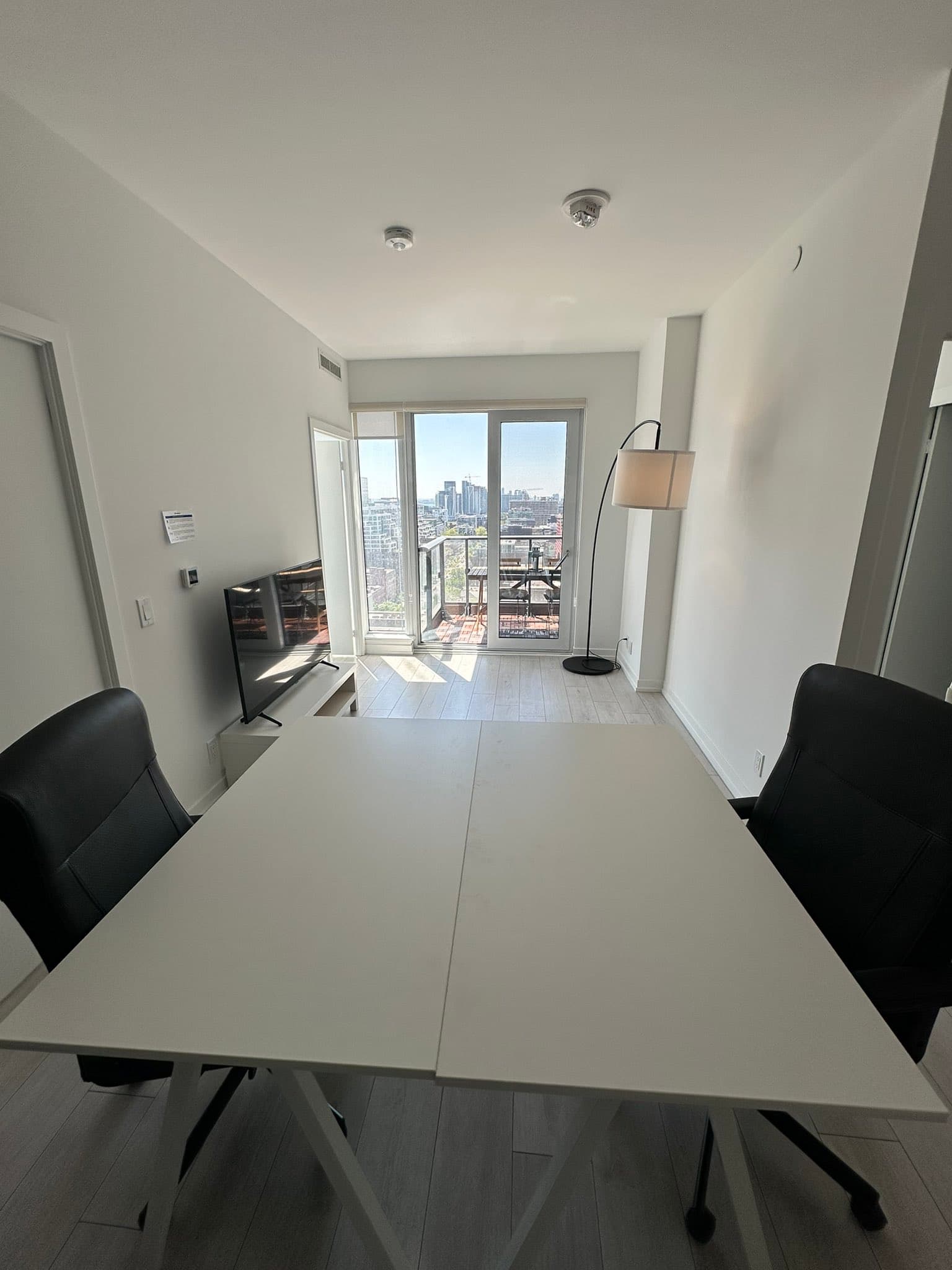 A furnished hacker condo room with a long shared desk, monitors and a view of the Toronto skyline